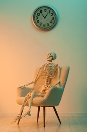 Waiting concept. Human skeleton sitting in armchair indoors