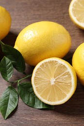Photo of Fresh lemons and green leaves on wooden table, closeup