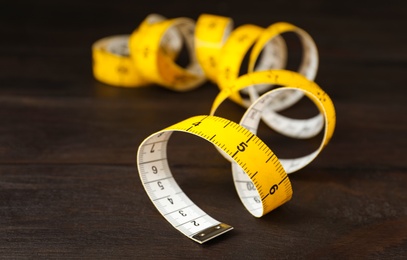 Yellow measuring tape on brown wooden table, closeup