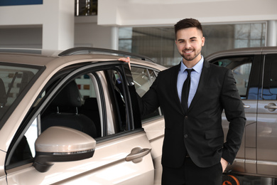 Photo of Young salesman near new car in dealership