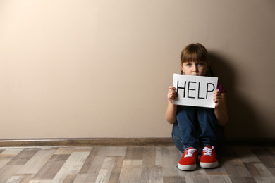 Sad little girl with sign HELP sitting on floor indoors, space for text. Child in danger