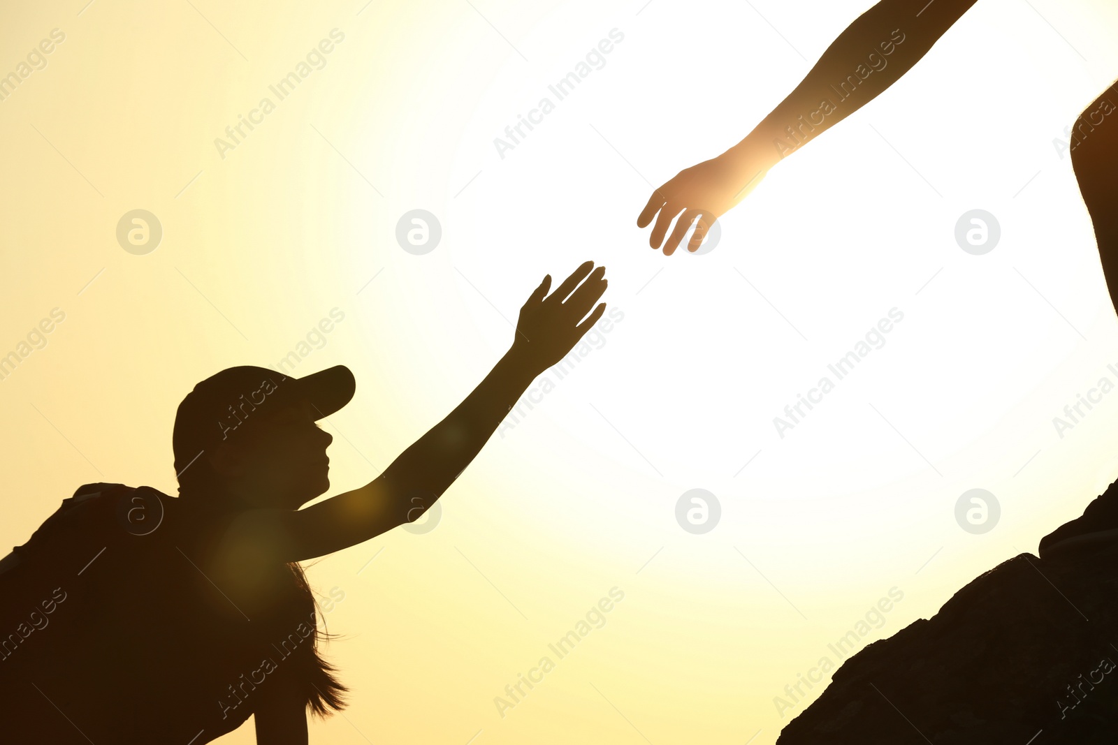 Photo of Silhouettes of man and woman helping each other to climb on hill against sunset