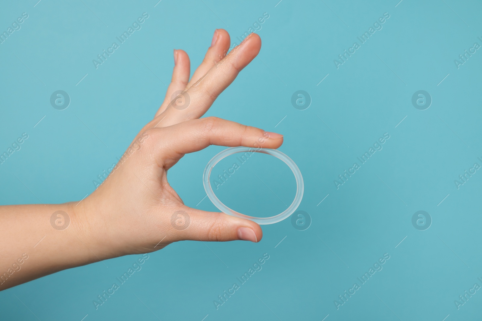 Photo of Woman holding diaphragm vaginal contraceptive ring on light blue background, closeup. Space for text