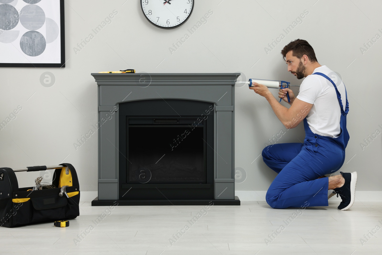 Photo of Professional technician sealing electric fireplace with caulk near white wall in room