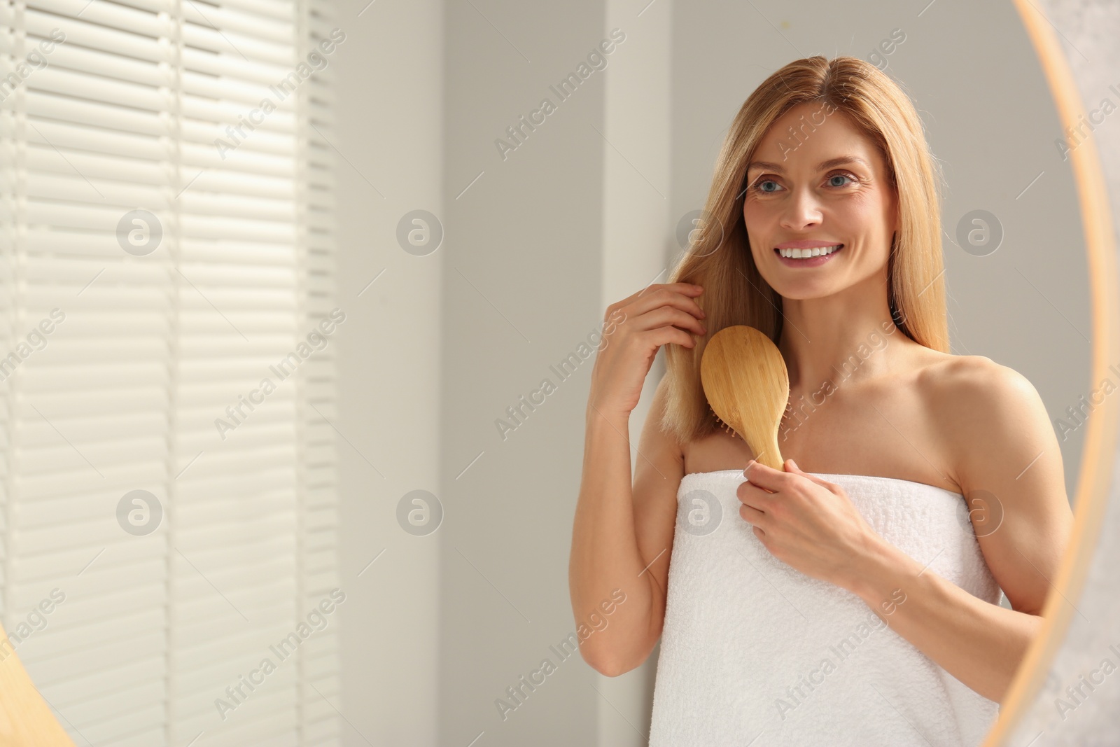 Photo of Beautiful woman brushing her hair near mirror in bathroom, space for text