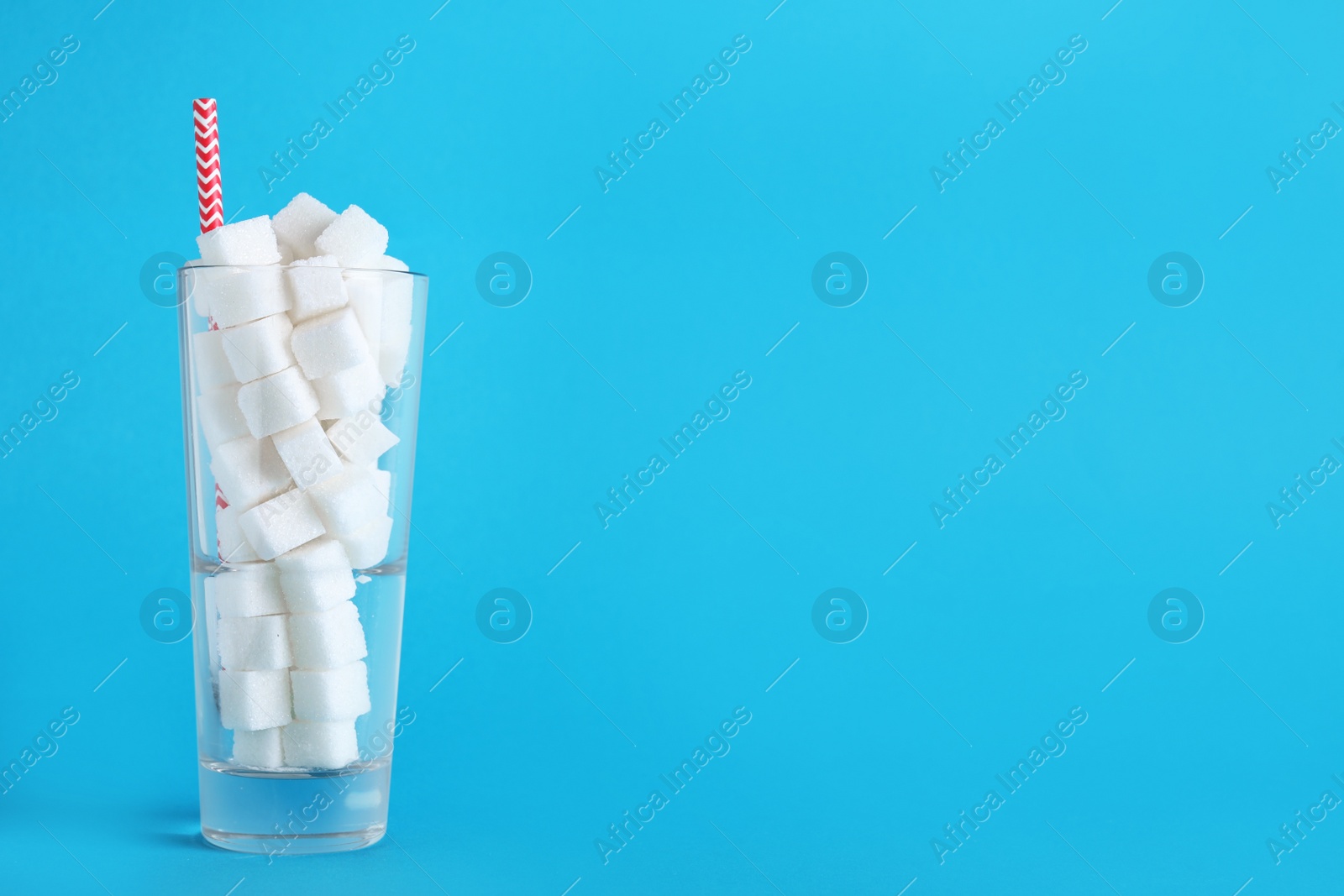 Photo of Refined sugar cubes in glass with straw on light blue background. Space for text