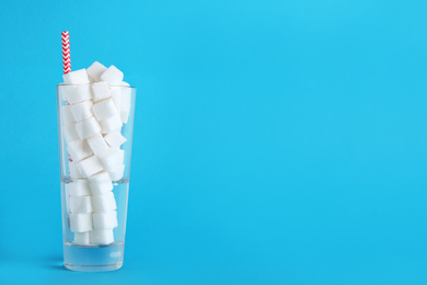 Refined sugar cubes in glass with straw on light blue background. Space for text