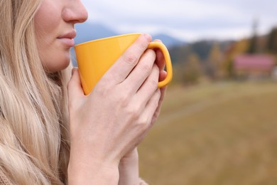 Photo of Young woman with mug of hot drink in mountains, closeup. Space for text