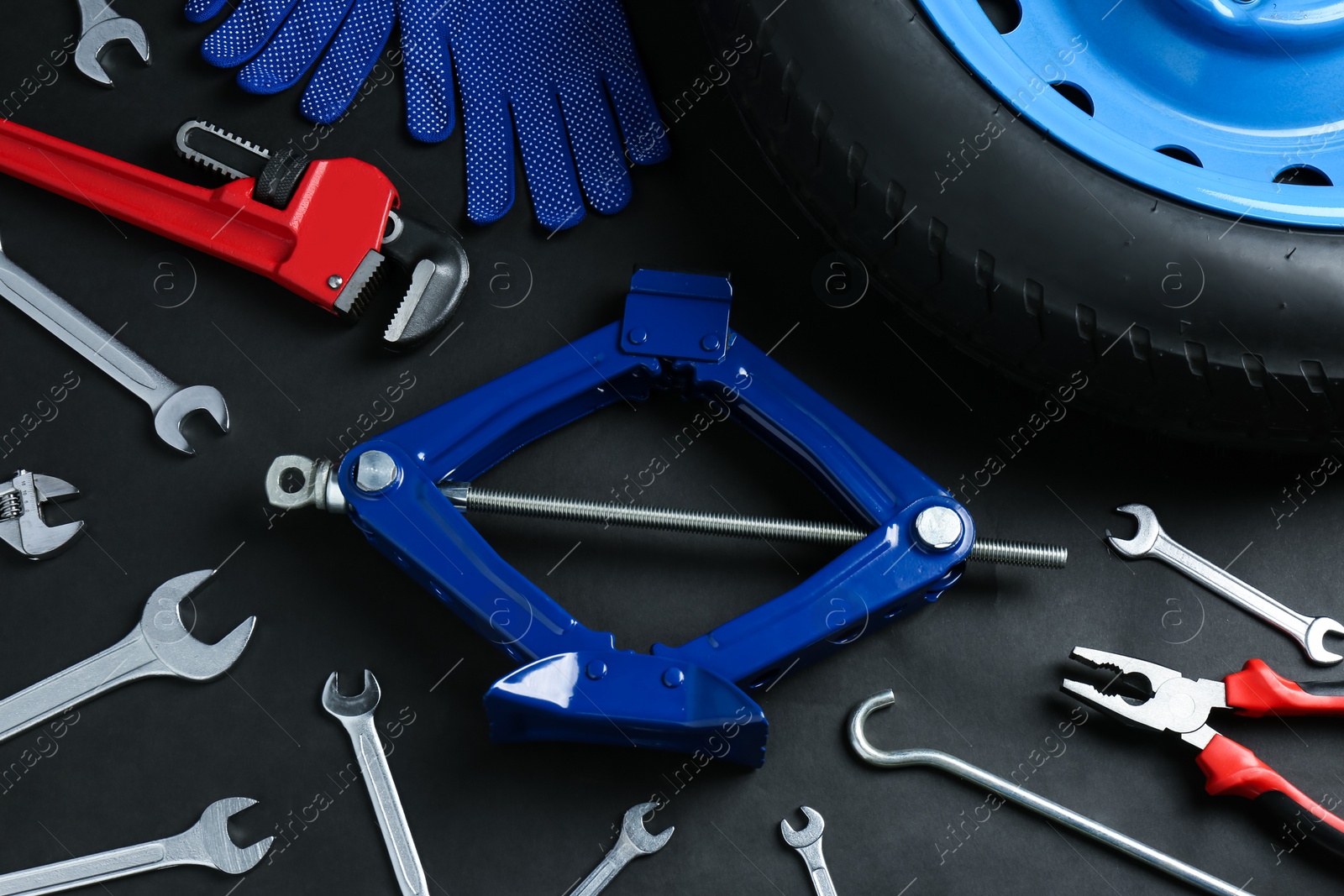 Photo of Car wheel, scissor jack, gloves and different tools on black background, flat lay