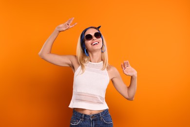 Photo of Portrait of smiling hippie woman in sunglasses dancing on orange background