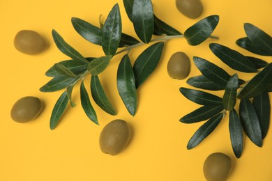 Fresh olives and green leaves on yellow background, flat lay