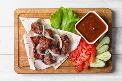 Wooden board with shish kebab and sauce on table, top view