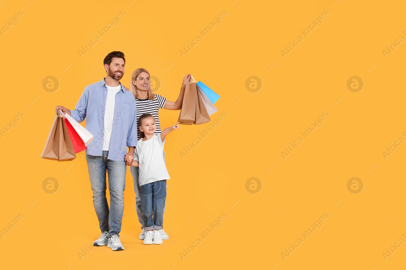 Photo of Family shopping. Happy parents and daughter with paper bags on orange background. Space for text