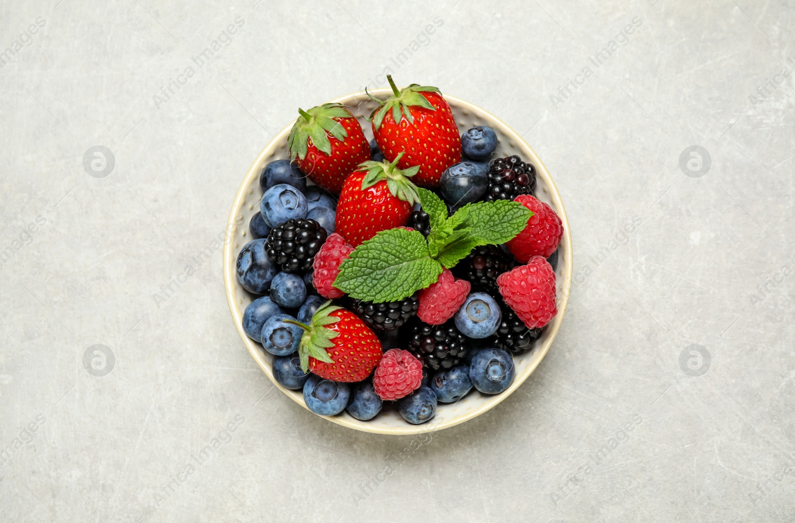 Photo of Mix of different fresh berries and mint in bowl on light grey table, top view