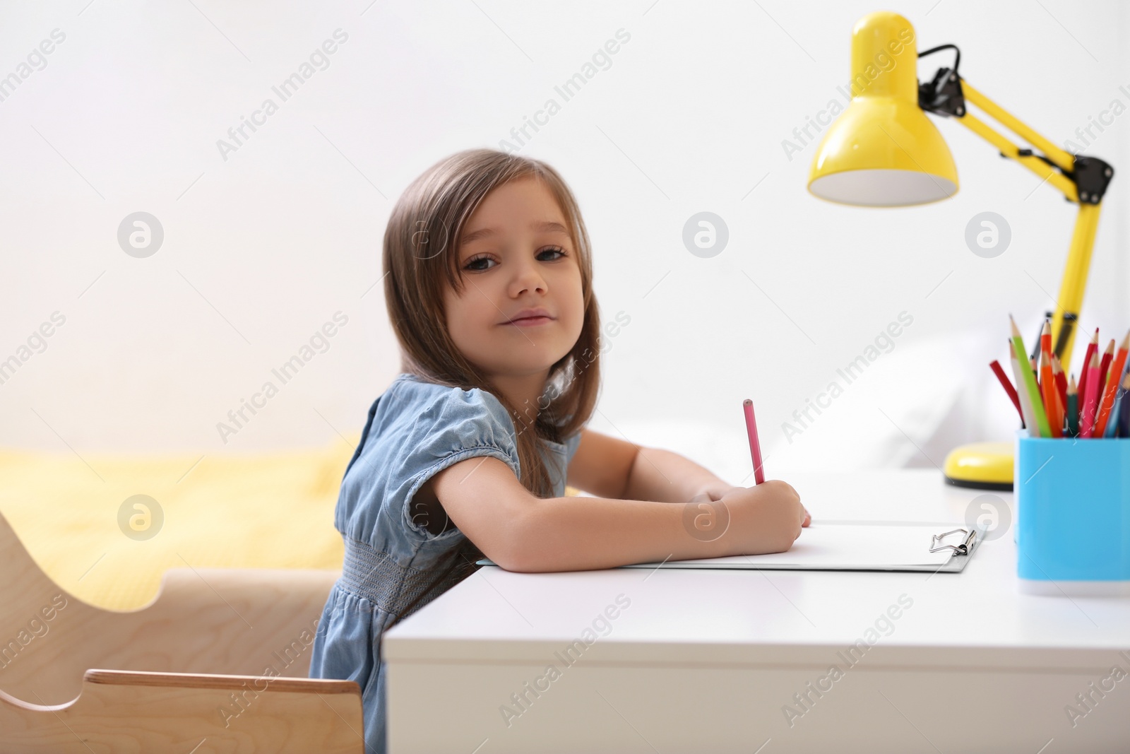 Photo of Cute little girl drawing at table in room