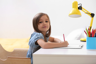 Cute little girl drawing at table in room