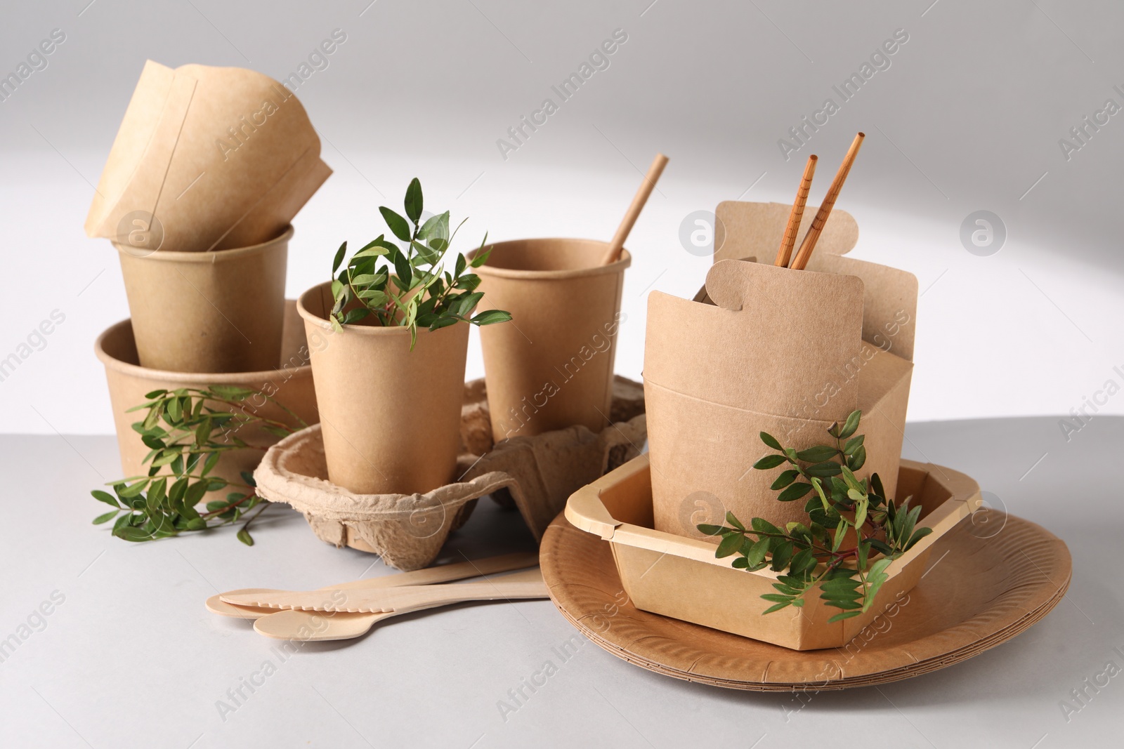 Photo of Eco friendly food packaging. Paper containers, tableware and green twigs on light background