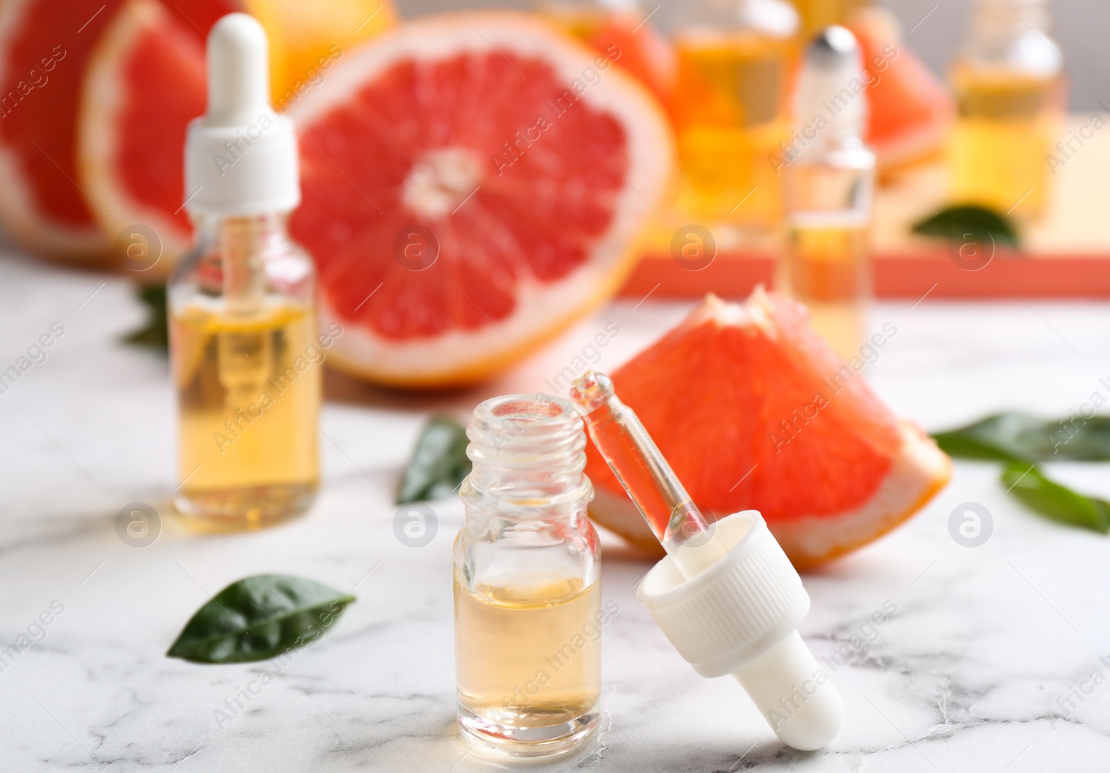 Photo of Bottles of essential oil and grapefruits on marble table