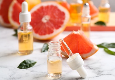 Bottles of essential oil and grapefruits on marble table