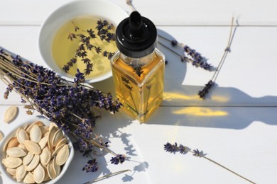 Healthy cooking oil, lavender flowers and pumpkin seeds on white wooden table, closeup