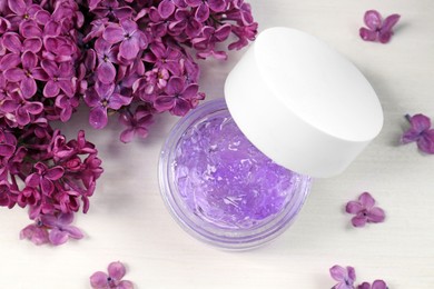 Photo of Jar of cosmetic product and lilac flowers on white wooden table, flat lay