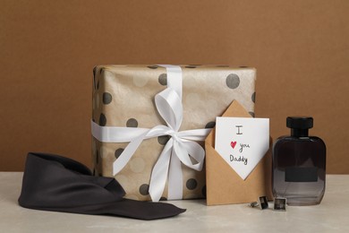 Happy Father's Day. Card with phrase I Love You, Daddy in envelope, cufflinks, perfume, tie and gift box on light marble table, closeup