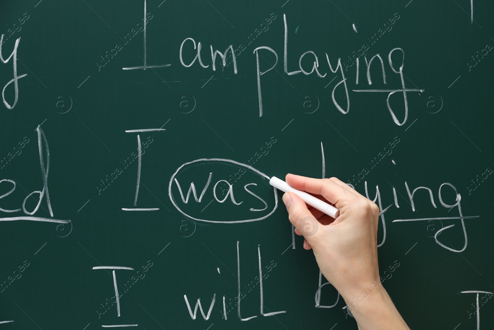 Photo of English teacher writing with chalk on green chalkboard, closeup