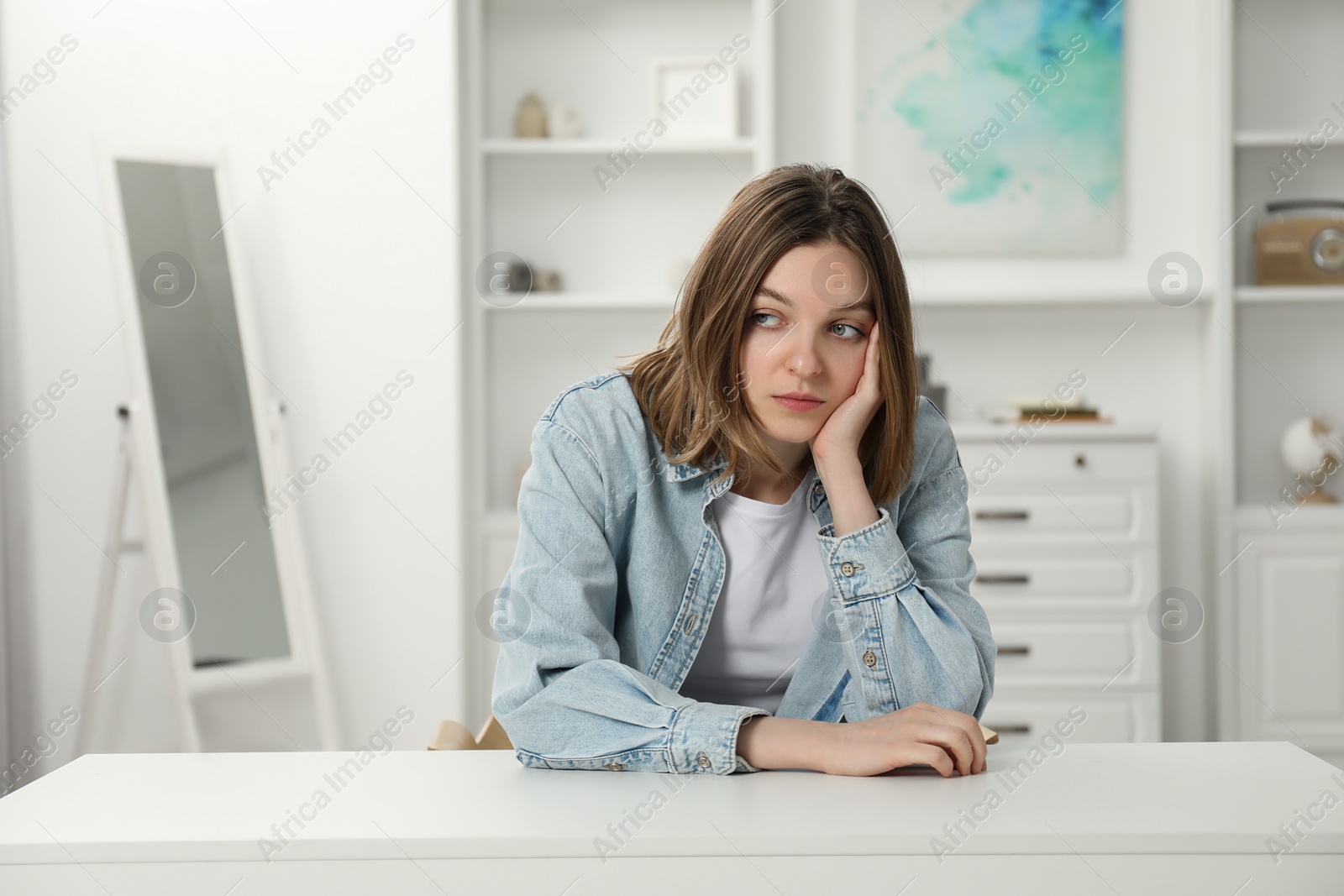 Photo of Sad young woman sitting at white table in room