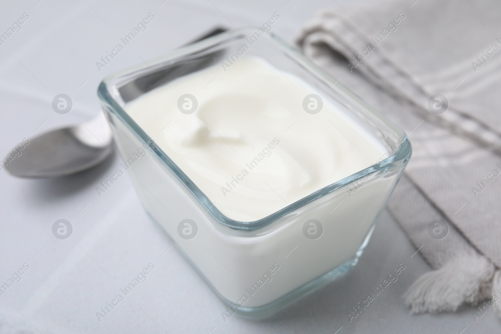 Photo of Delicious natural yogurt in glass bowl and spoon on white table, closeup