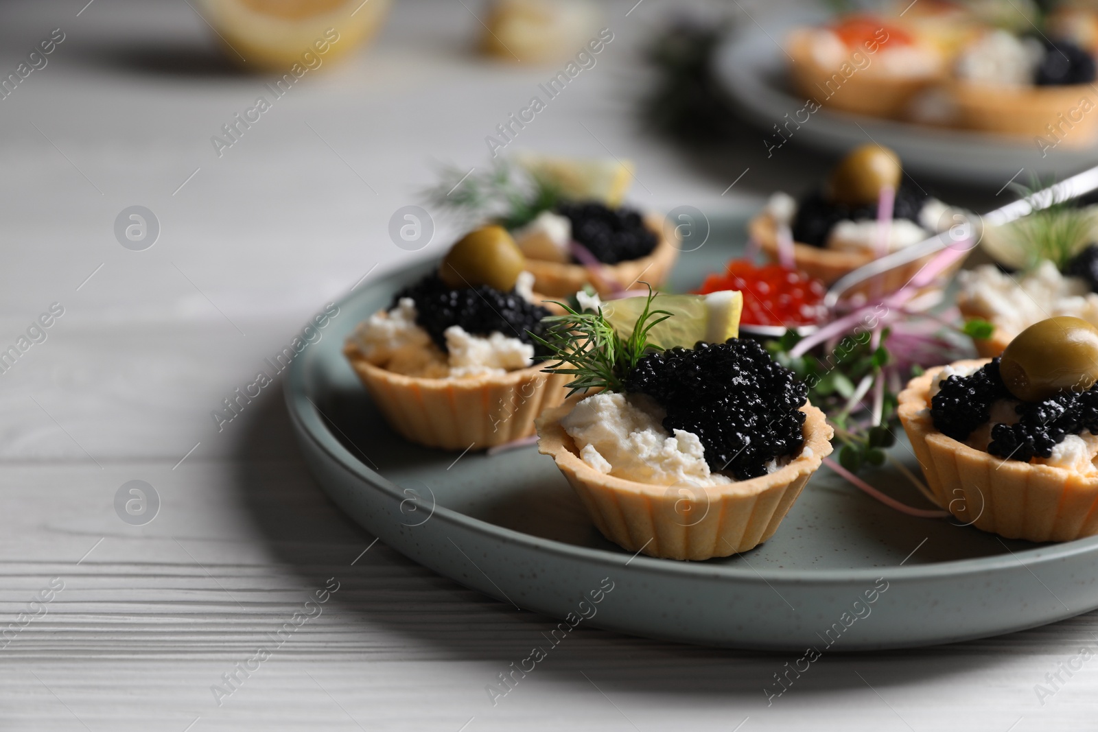 Photo of Delicious tartlets with caviar and cream cheese served on white wooden table, closeup