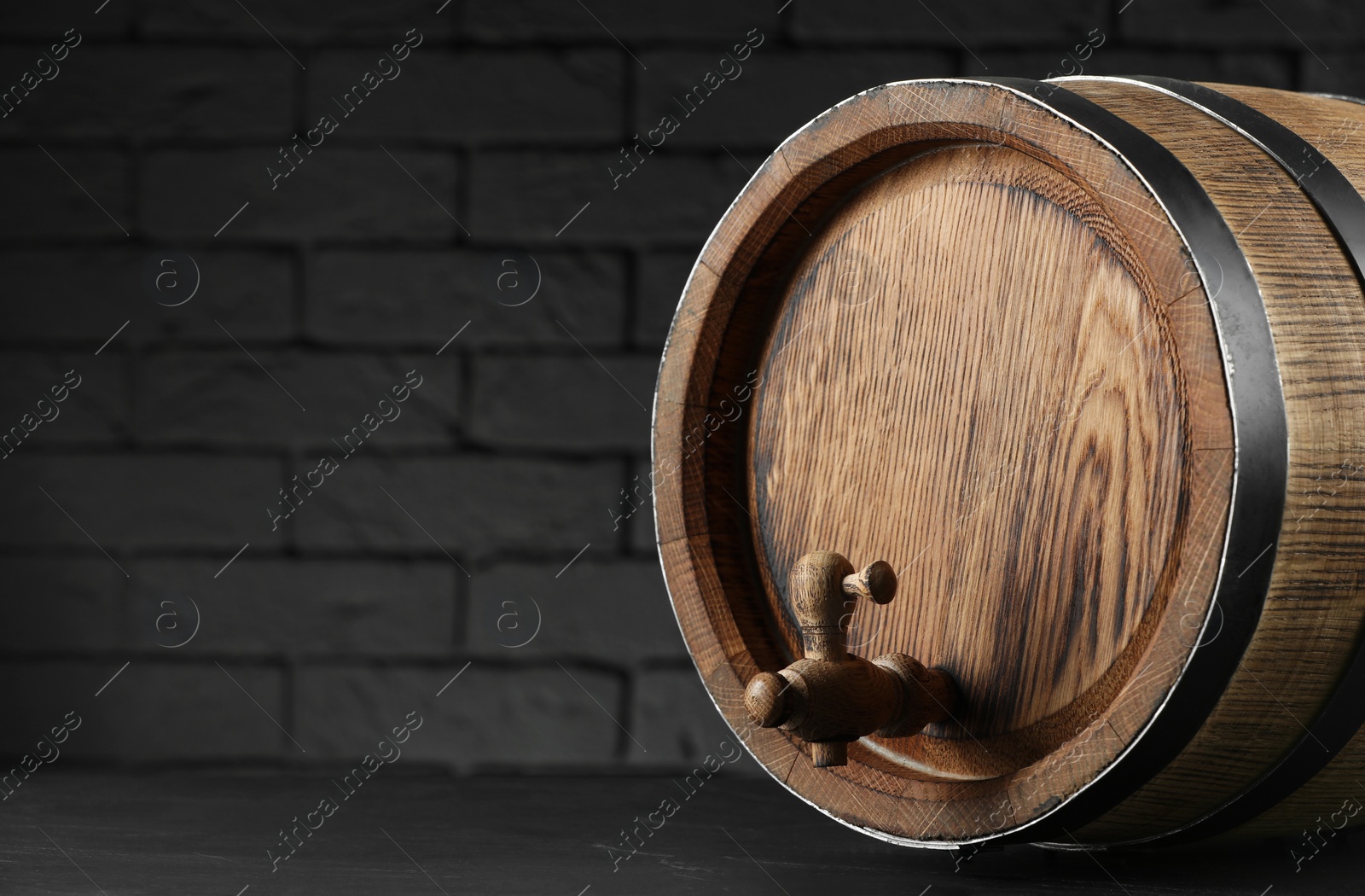 Photo of One wooden barrel with tap on table near brick wall, closeup. Space for text