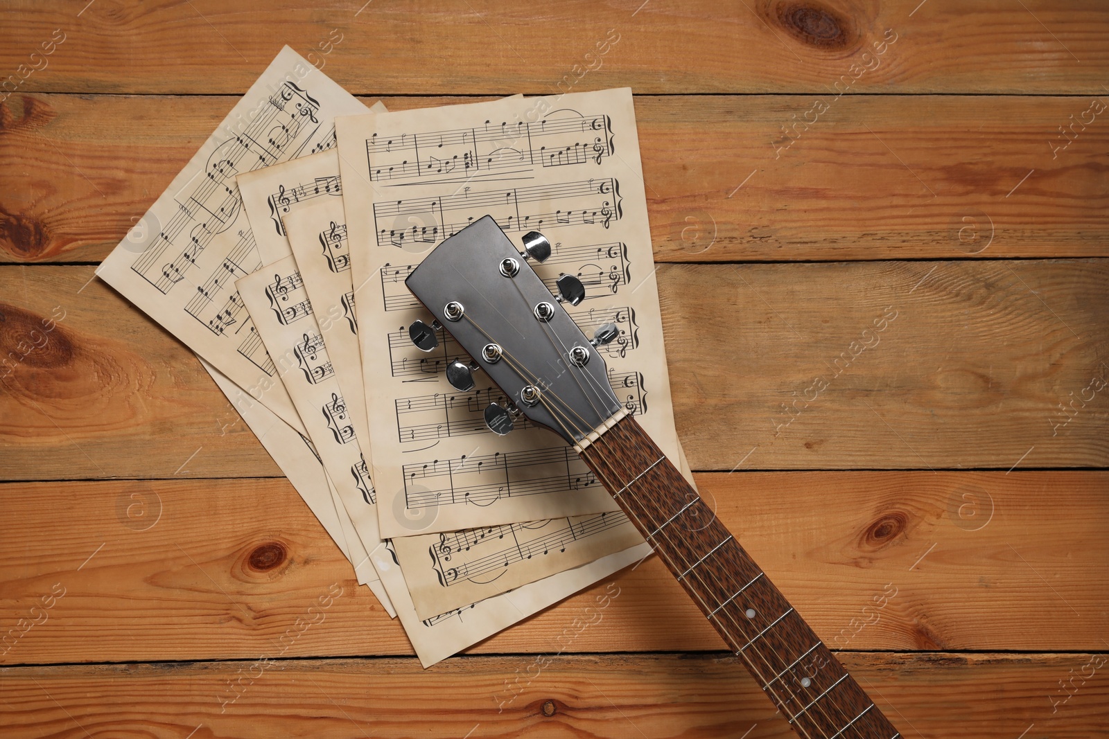 Photo of Paper sheets with music notes and acoustic guitar on wooden table, top view