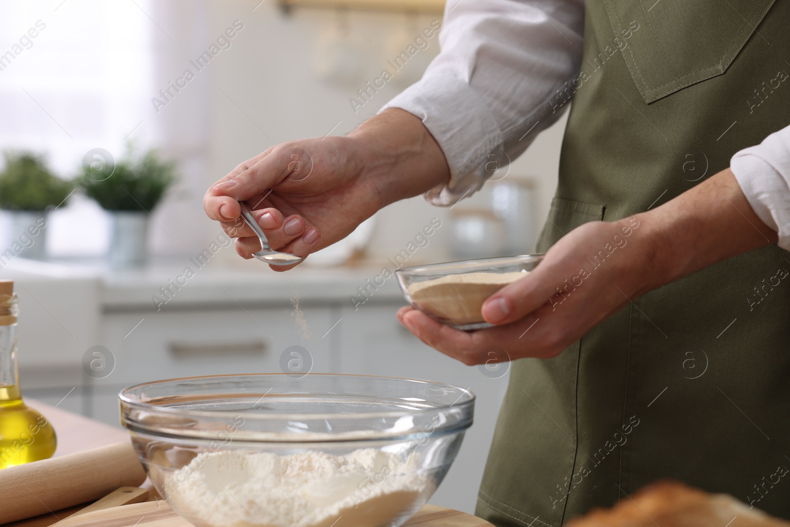 Photo of Making bread. Man putting dry yeast into bowl with flour at wooden table in kitchen, closeup