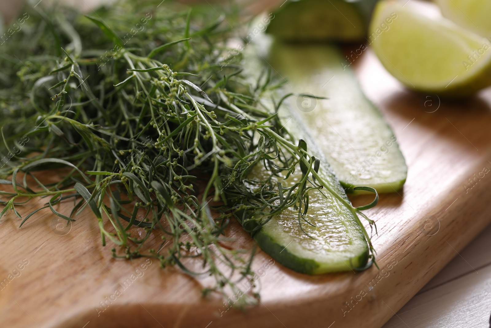 Photo of Fresh tarragon leaves and slices of cucumber on wooden board, closeup