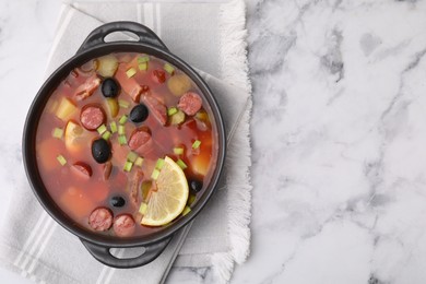 Photo of Meat solyanka soup with thin dry smoked sausages in bowl on white marble table, top view. Space for text