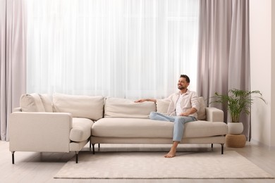 Photo of Happy man resting on sofa near window with beautiful curtains in living room