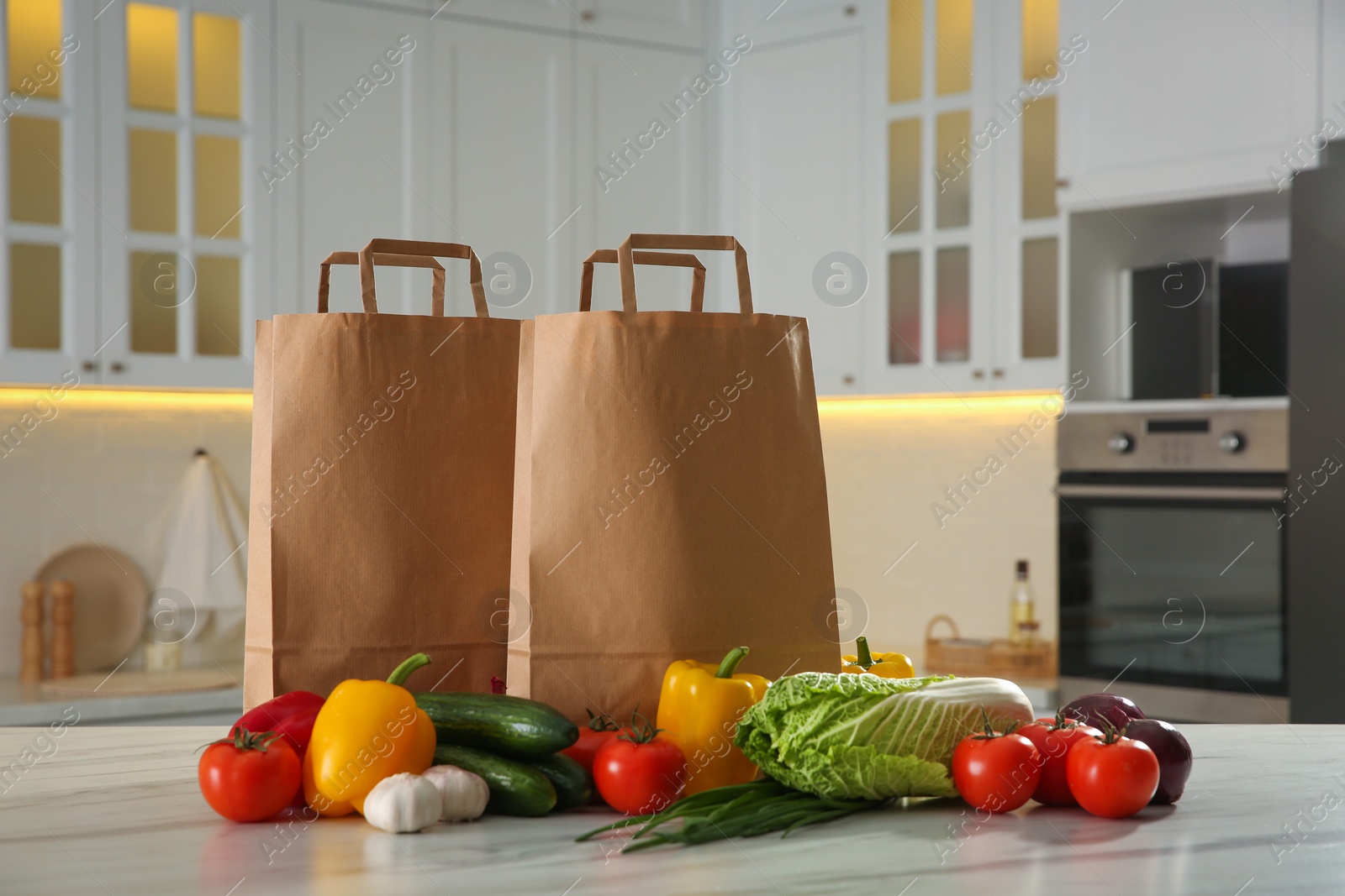 Photo of Paper shopping bags and fresh vegetables on white marble table in kitchen