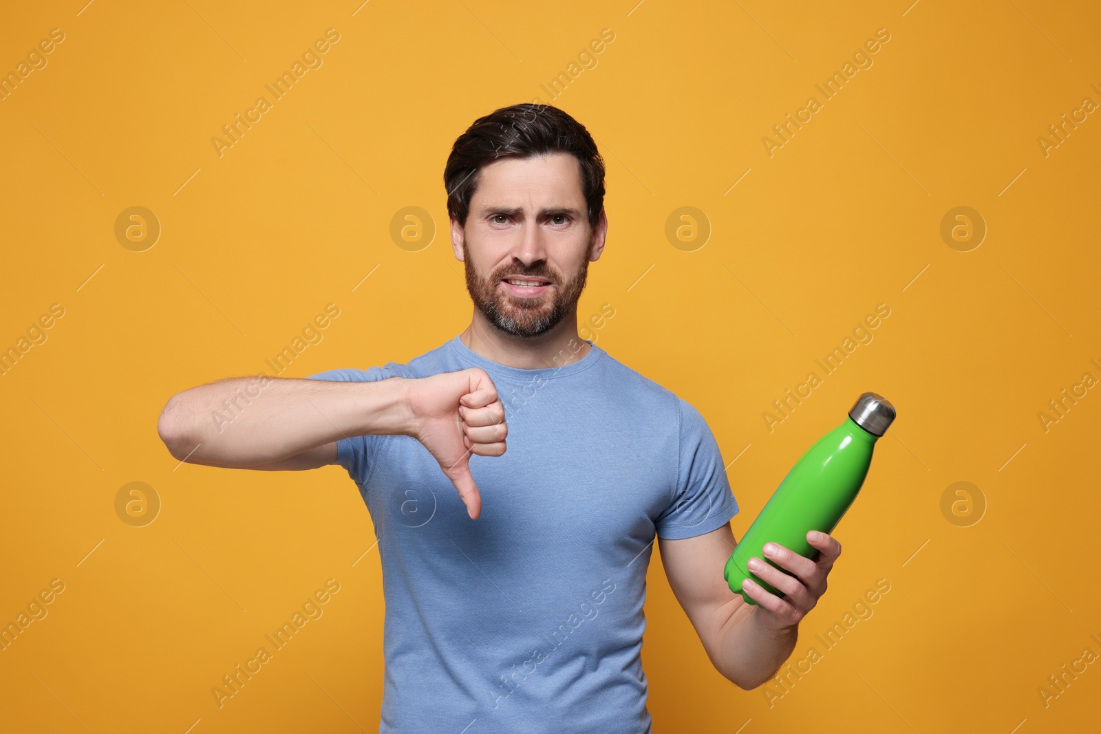 Photo of Man with green thermo bottle showing thumbs down on orange background