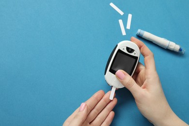 Photo of Diabetes. Woman checking blood sugar level with glucometer on blue background, top view. Space for text