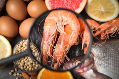 Photo of Different products with magnifier focused on shrimps, closeup. Food allergy concept