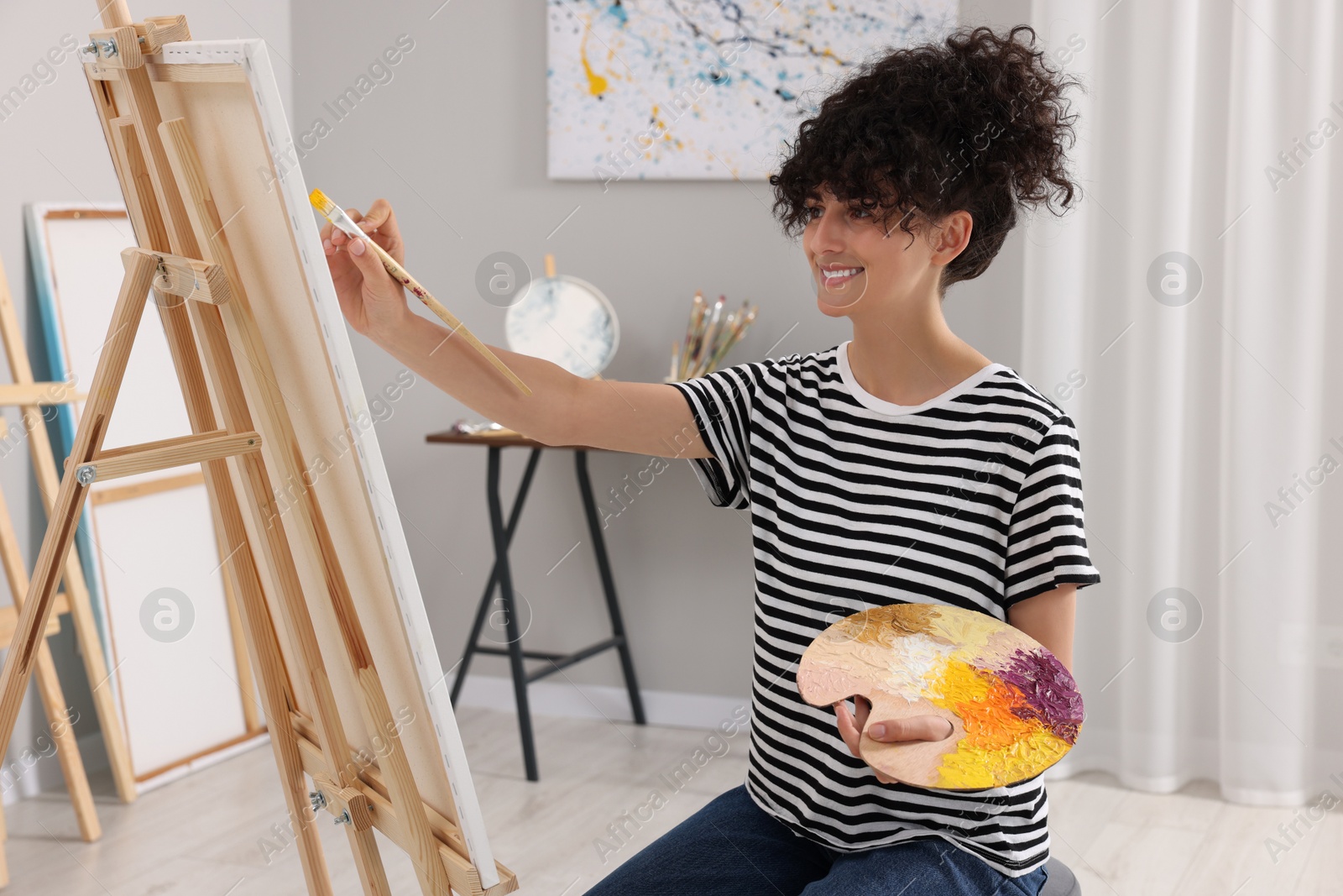 Photo of Young woman painting on easel with canvas in studio