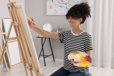 Young woman painting on easel with canvas in studio