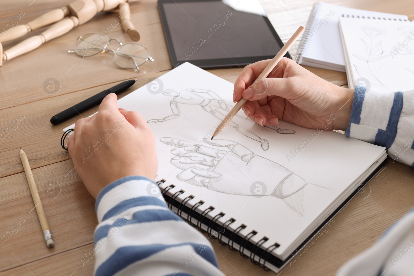 Photo of Woman drawing in sketchbook with pencil at wooden table, closeup