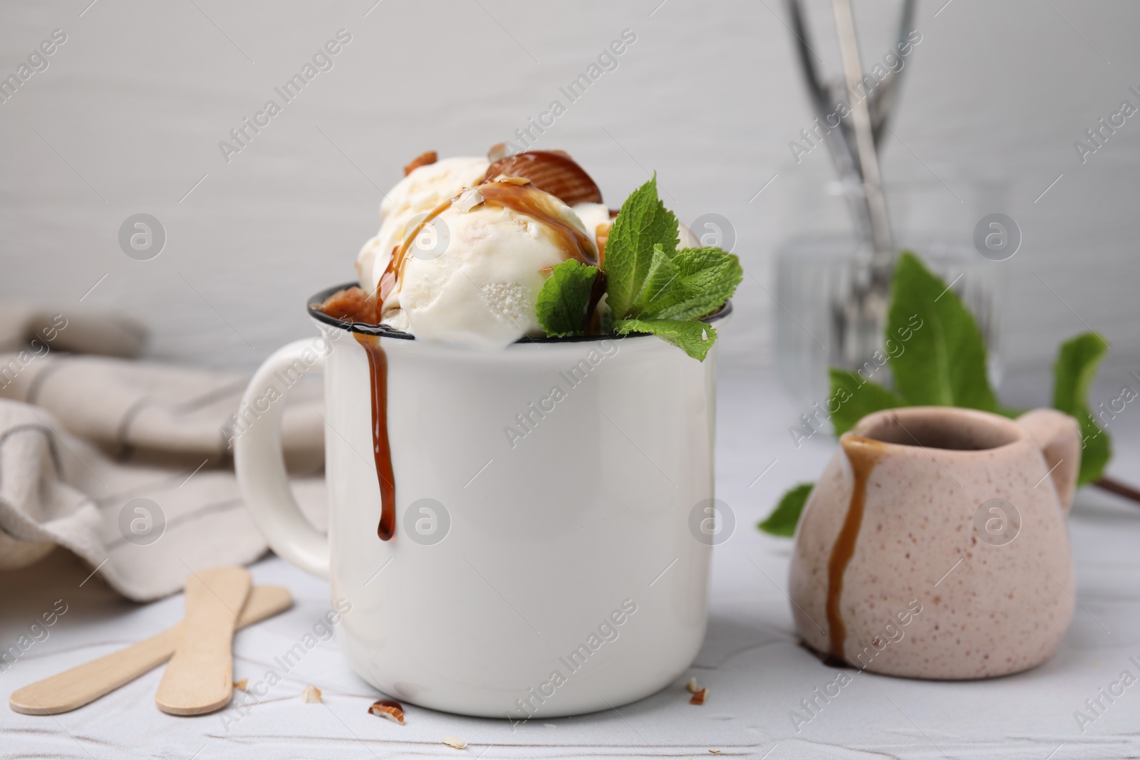 Photo of Scoops of ice cream with caramel sauce, candies and mint leaves on white textured table, closeup
