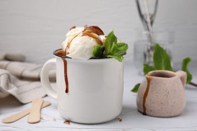 Photo of Scoopsice cream with caramel sauce, candies and mint leaves on white textured table, closeup