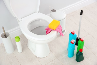 Ceramic toilet bowl, bottles of detergent and cleaning supplies in modern bathroom