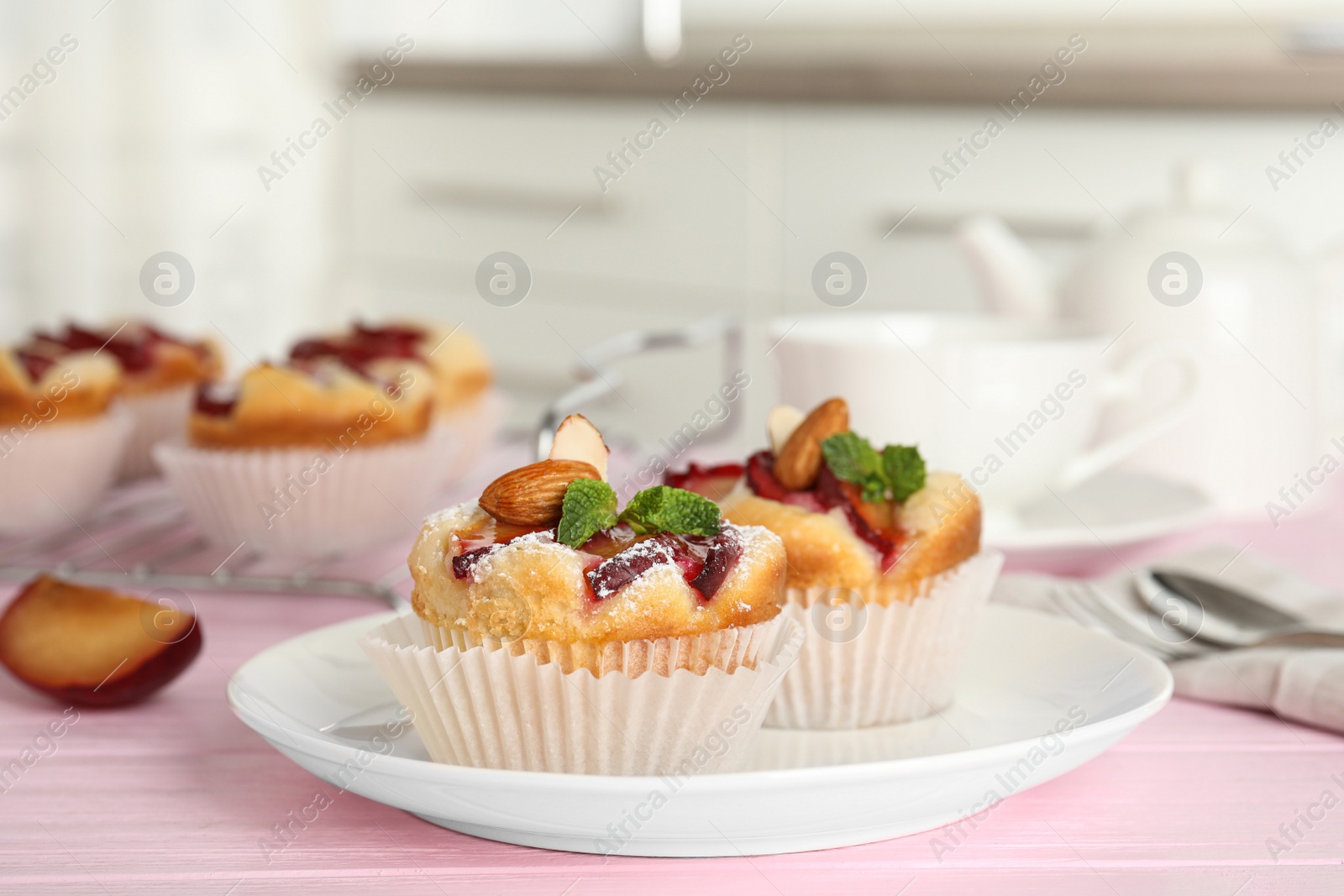 Photo of Delicious cupcakes with plums on pink wooden table, closeup