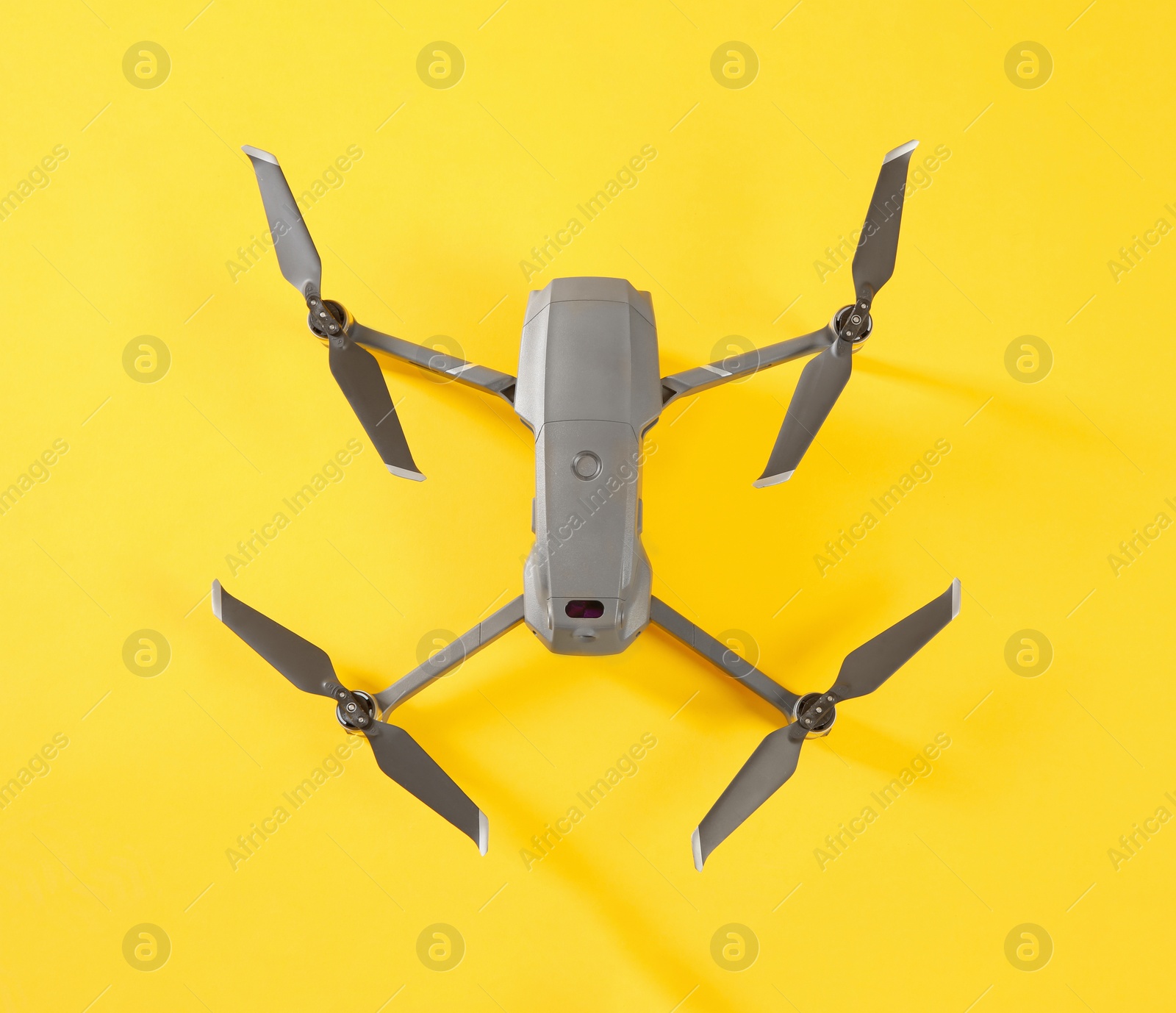 Photo of Modern drone with camera on yellow background, top view