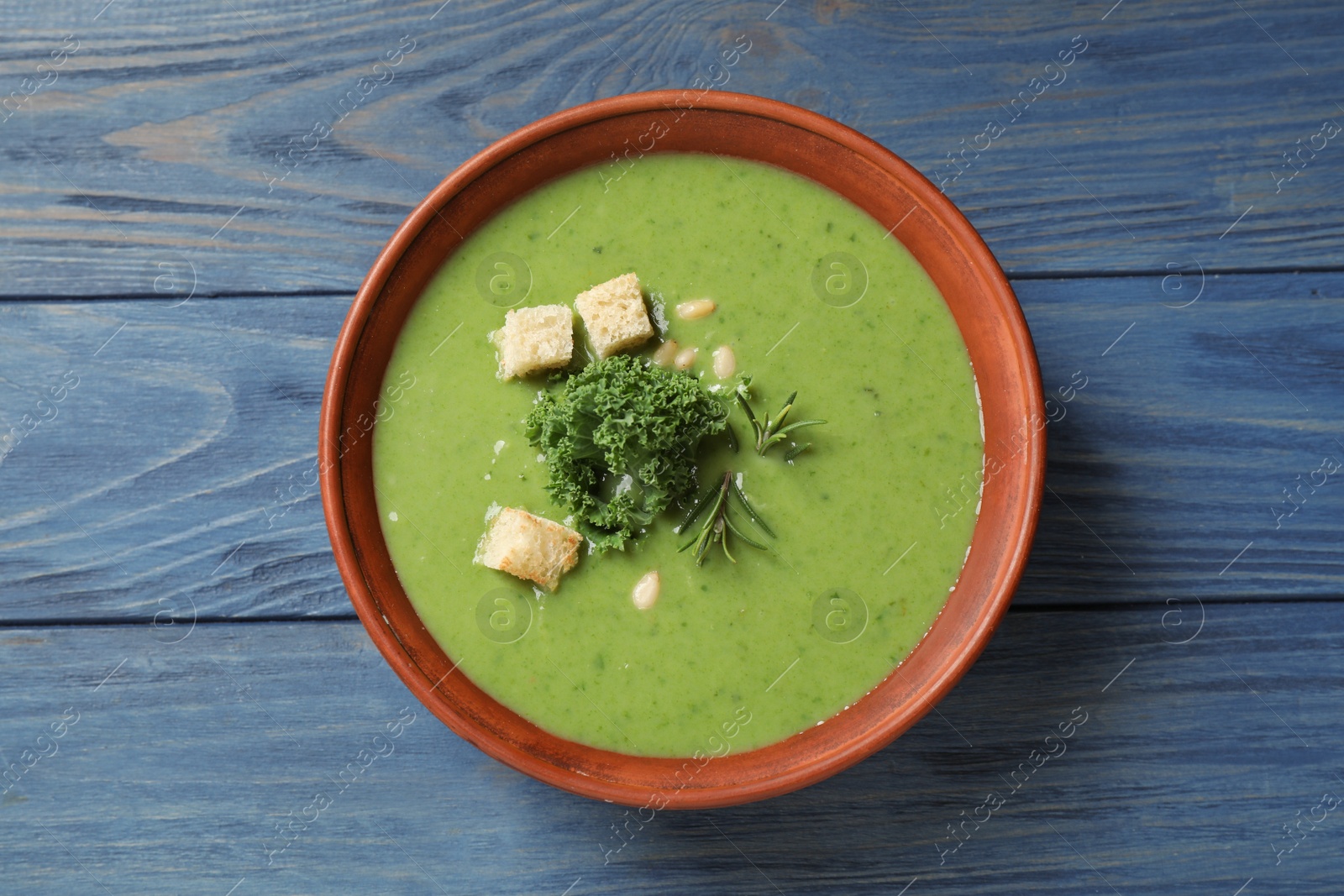 Photo of Tasty kale soup with croutons on blue wooden table, top view