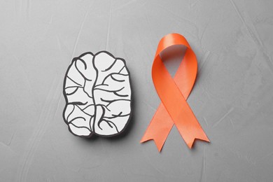Photo of Orange ribbon and paper brain cutout on light grey table, flat lay. Multiple sclerosis awareness